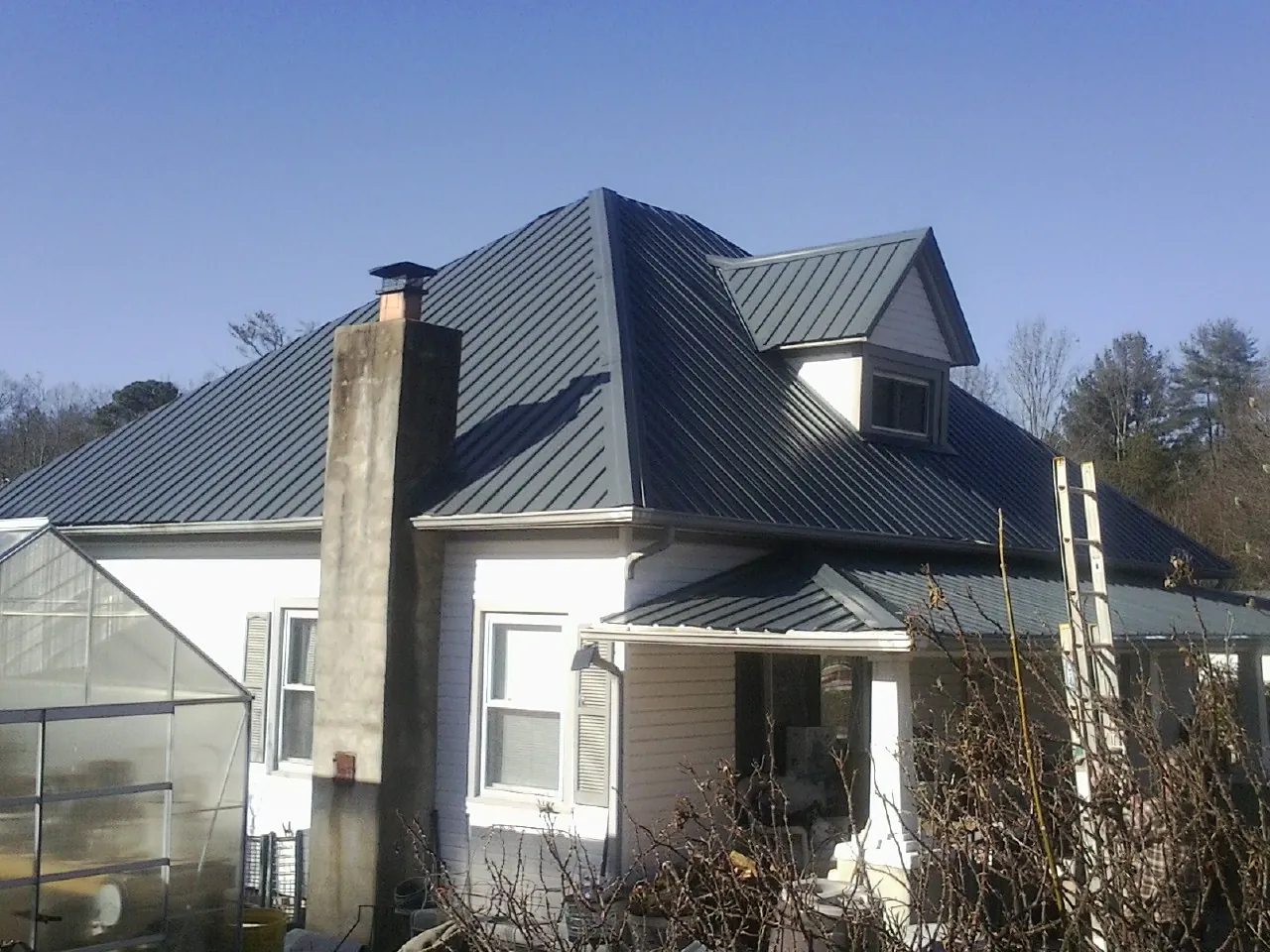 Dark blue standing seam metal roof on a white farmhouse with dormer — Slate & Tile Roof Repair by Roofing Brothers in Lavinia