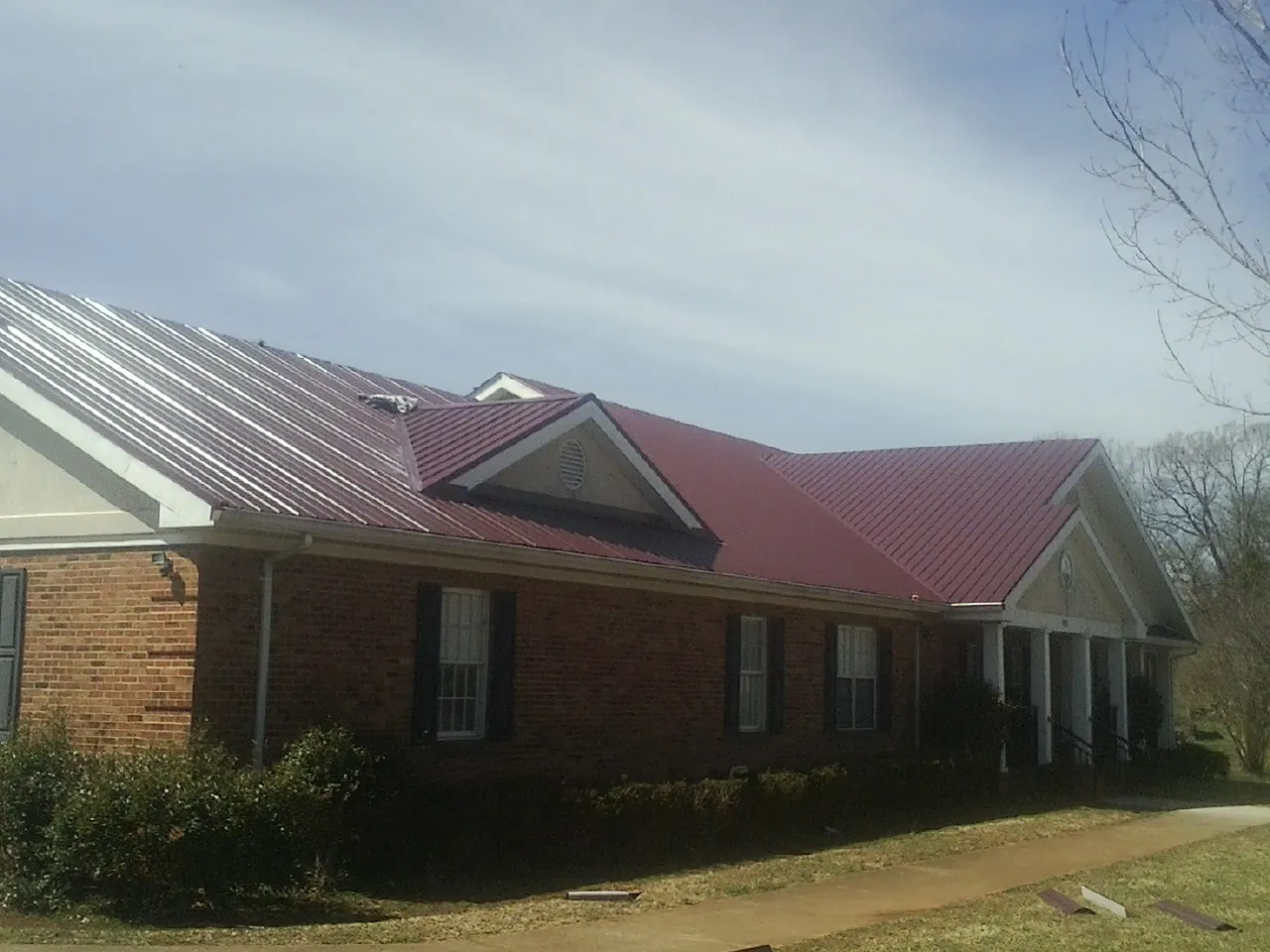 Red metal roof with gabled entries on a long brick building, from a Hail Damage Roof Repair job in Lavinia