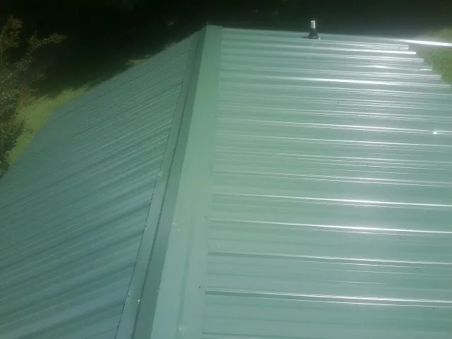 New green metal panels meeting at the ridge of a roof — Flat Roof Repair work by our crew in Lavinia