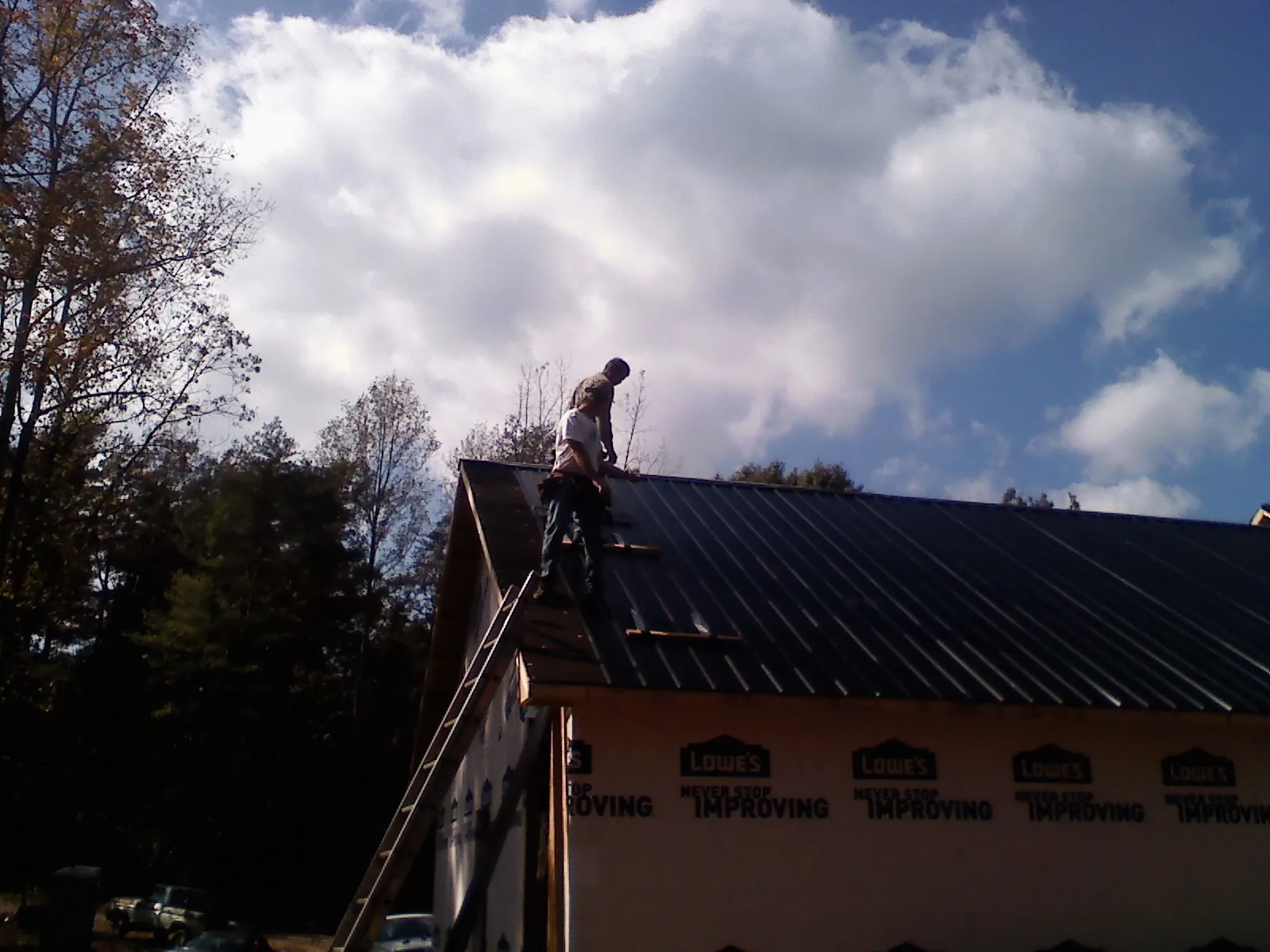 Roofer fastening dark metal panels high against a cloudy sky, from a Roof Inspection job in Lavinia