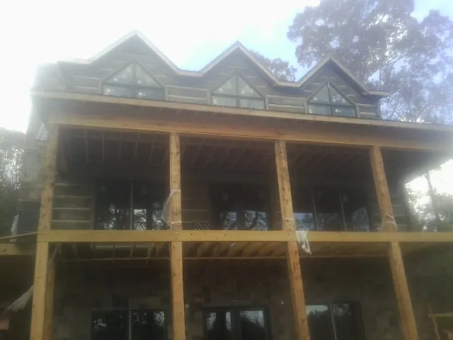 Dormers and porch framing on a large log home under construction — Roof Coating work by our crew in Lavinia
