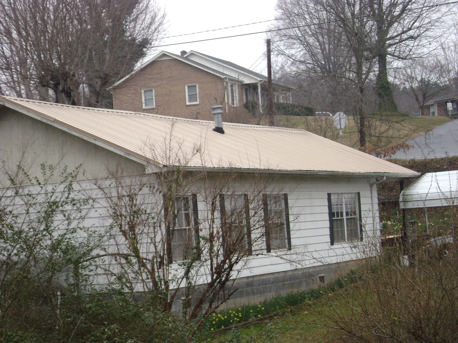 Tan metal roof on a white sided house set into a hillside — Commercial Roofing by Roofing Brothers in Lavinia