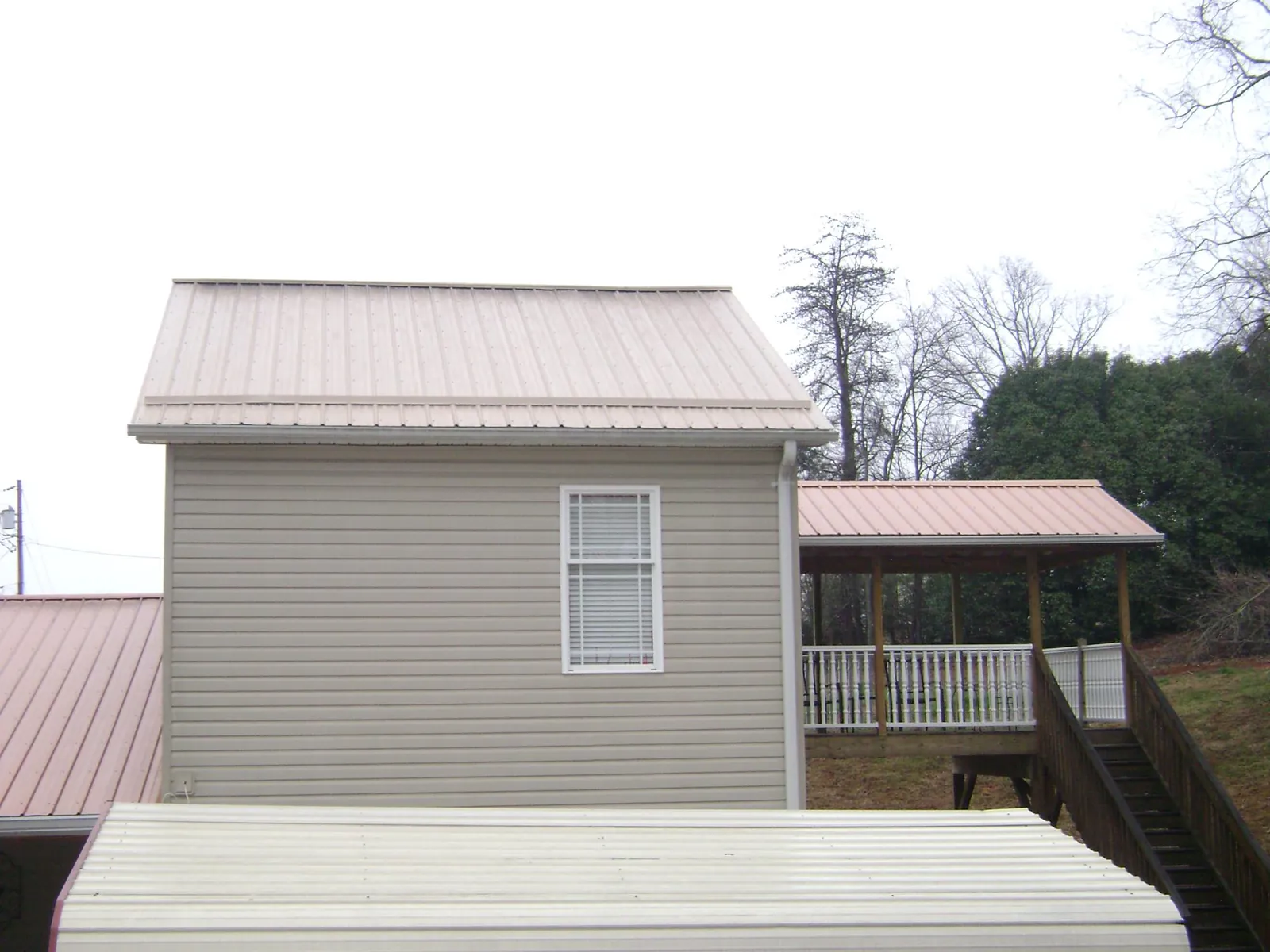 Tan metal roofs on a two story addition and attached porch, from a Roof Replacement job in Lavinia
